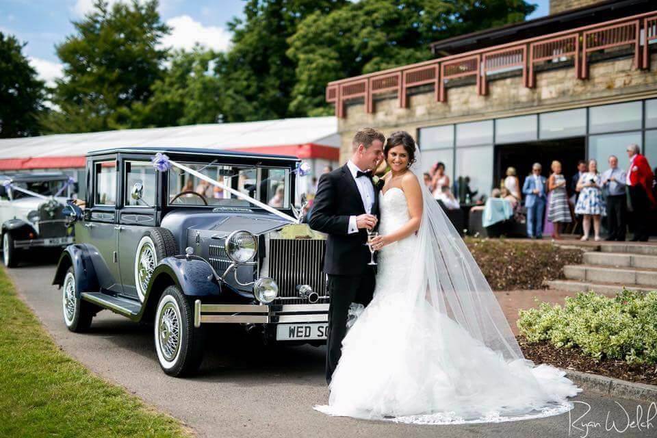 Happy couple celebrating wedding outside venue with viscount classic wedding car