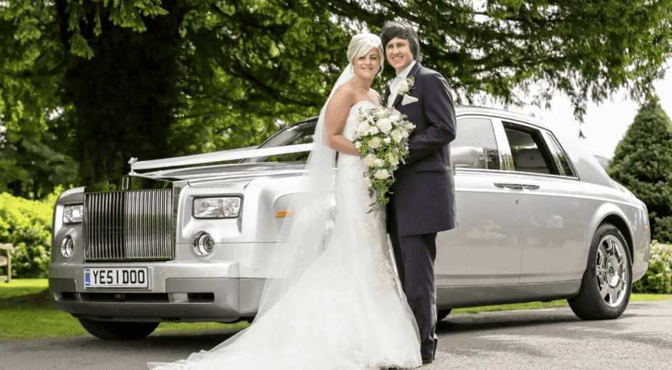 bride and groom with white flowers hvaing wedding photography next to rolls royce phantom